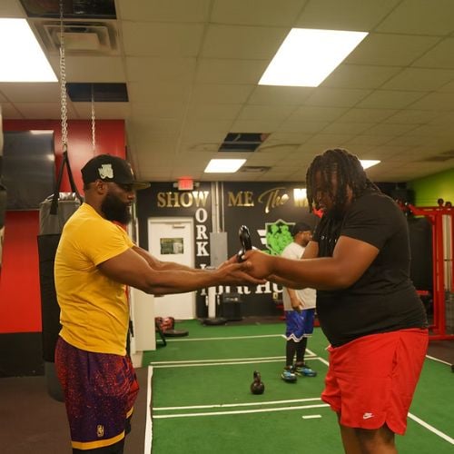 Two people fist bumping in a fitness gym with kettlebells nearby