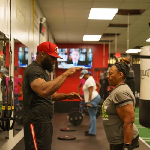 Fitness trainer coaching client in gym with red and green workout space