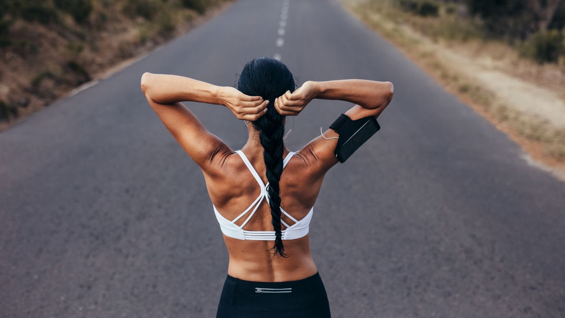 Athlete adjusting earphones on empty road, back view of fitness training