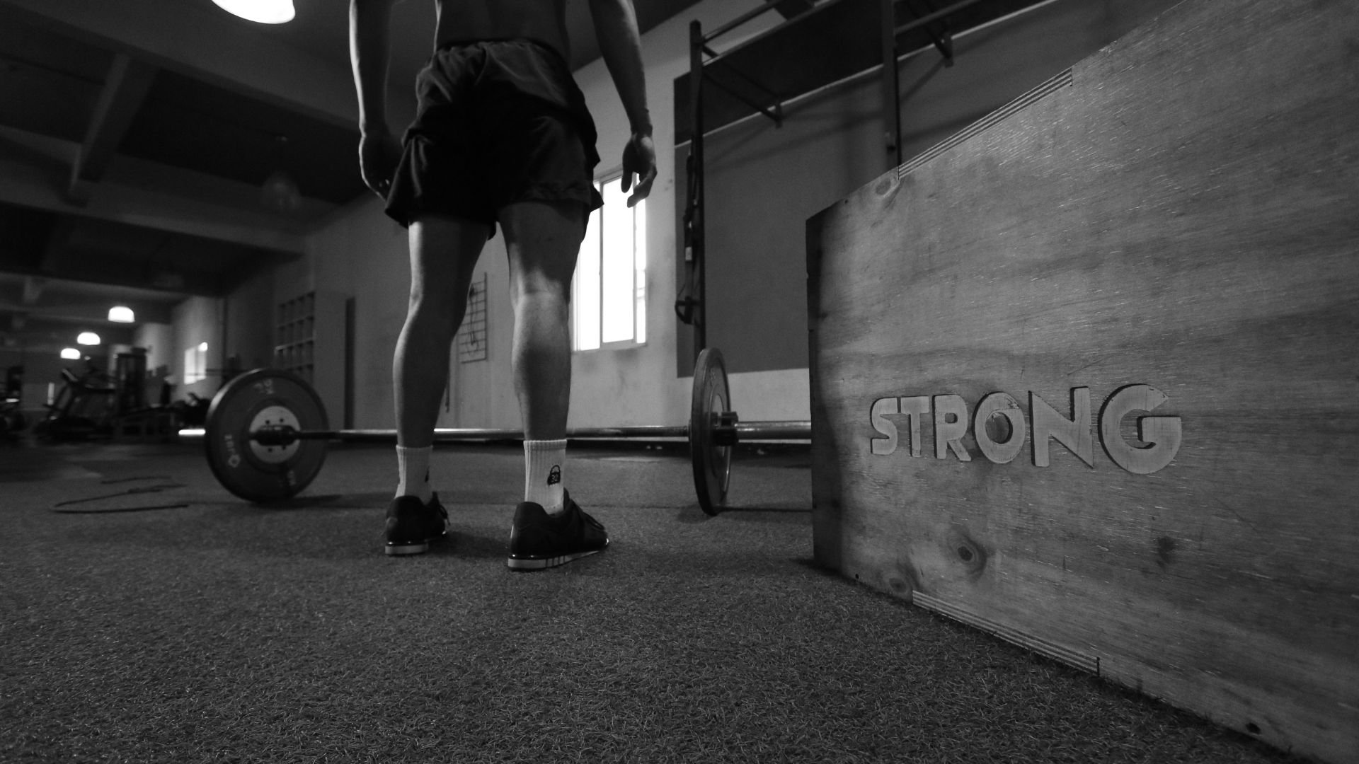 Athlete preparing to lift barbell in gym with 'Strong' sign