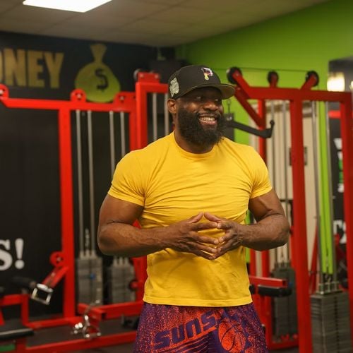 Muscular man in yellow shirt smiling in colorful gym with exercise equipment