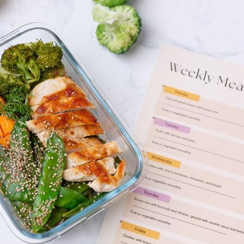 Meal prep container with sliced chicken, broccoli, and weekly meal planner